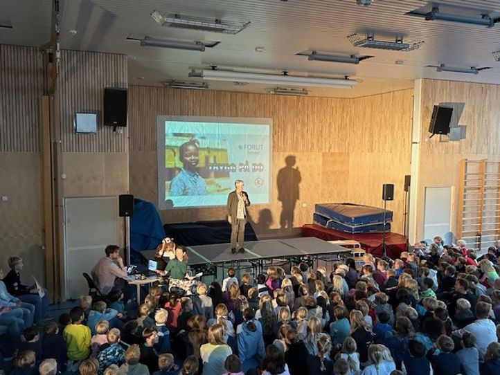 en gruppe mennesker som sitter i et rom med en scene og en skjerm