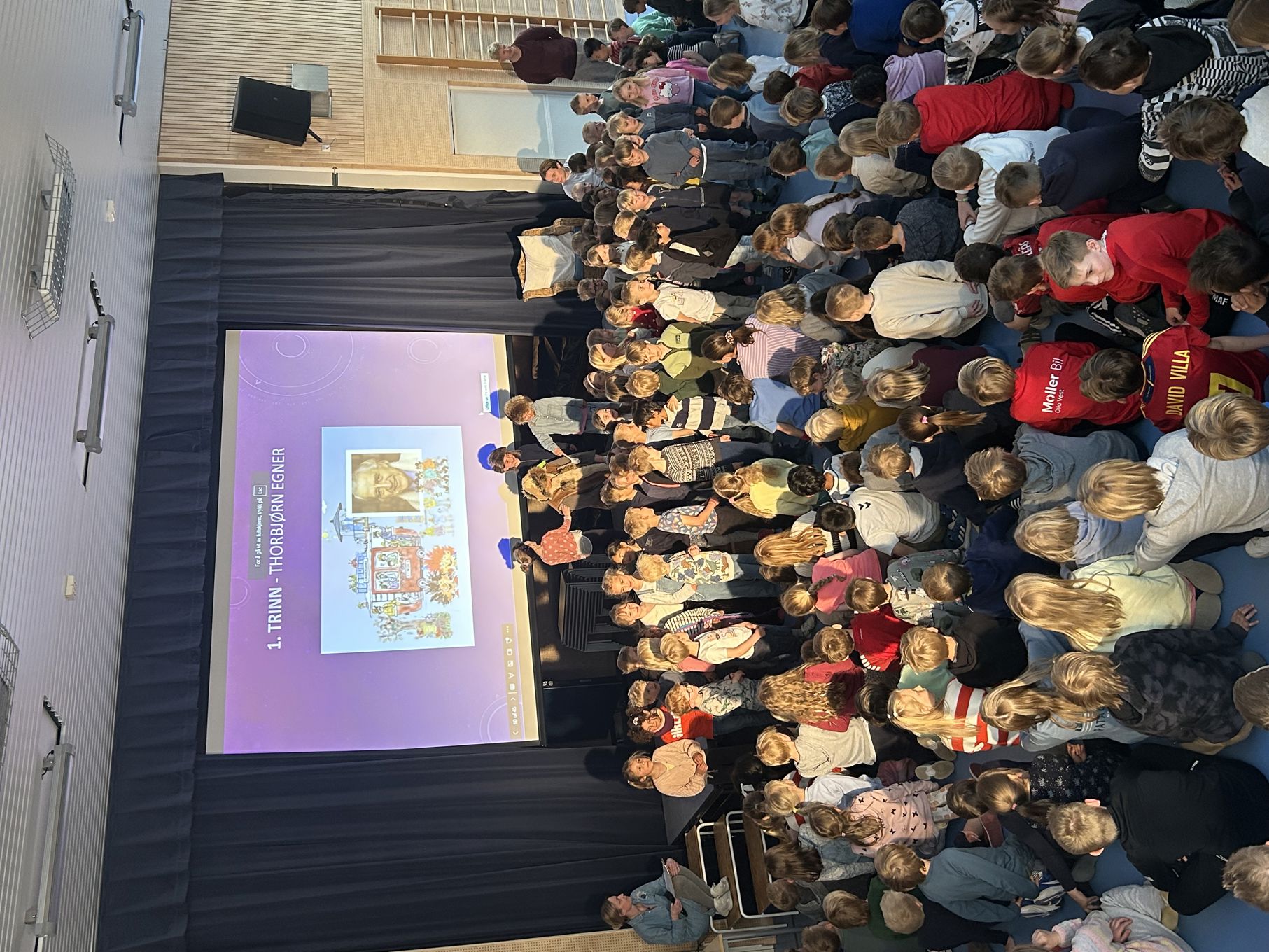 en gruppe mennesker som sitter i et rom med en stor skjerm en gruppe mennesker som sitter i et rom med en stor skjerm